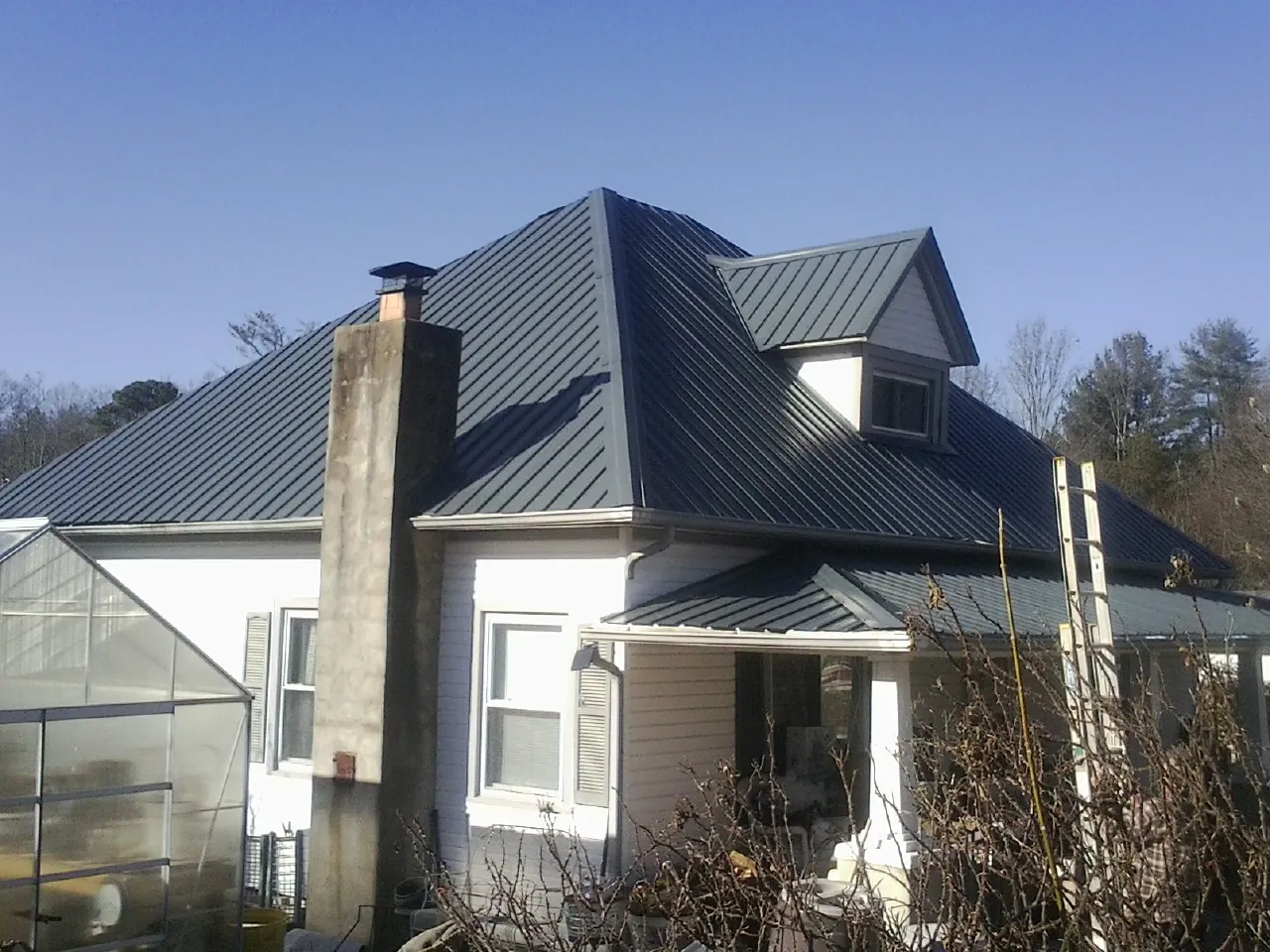 Dark blue standing seam metal roof on a white farmhouse with dormer — Slate & Tile Roof Repair by Roofing Brothers in Gifford