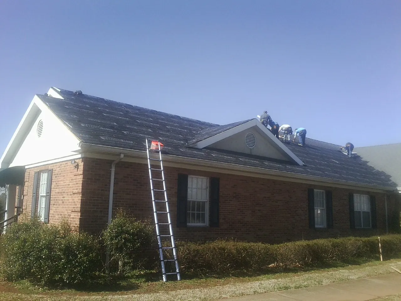Crew tearing shingles off a brick ranch roof with a ladder set — Metal Roof Repair work by our crew in Gifford