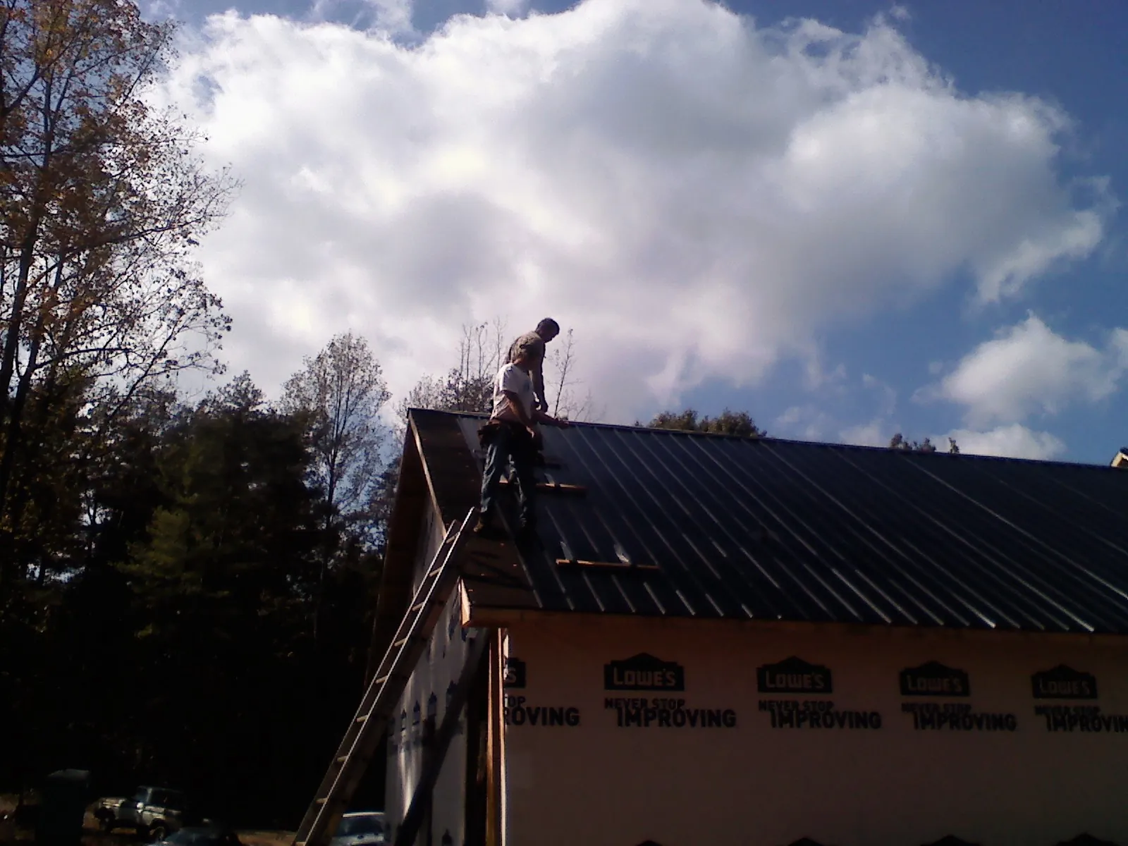 Roofer fastening dark metal panels high against a cloudy sky, from a Roof Inspection job in Gifford