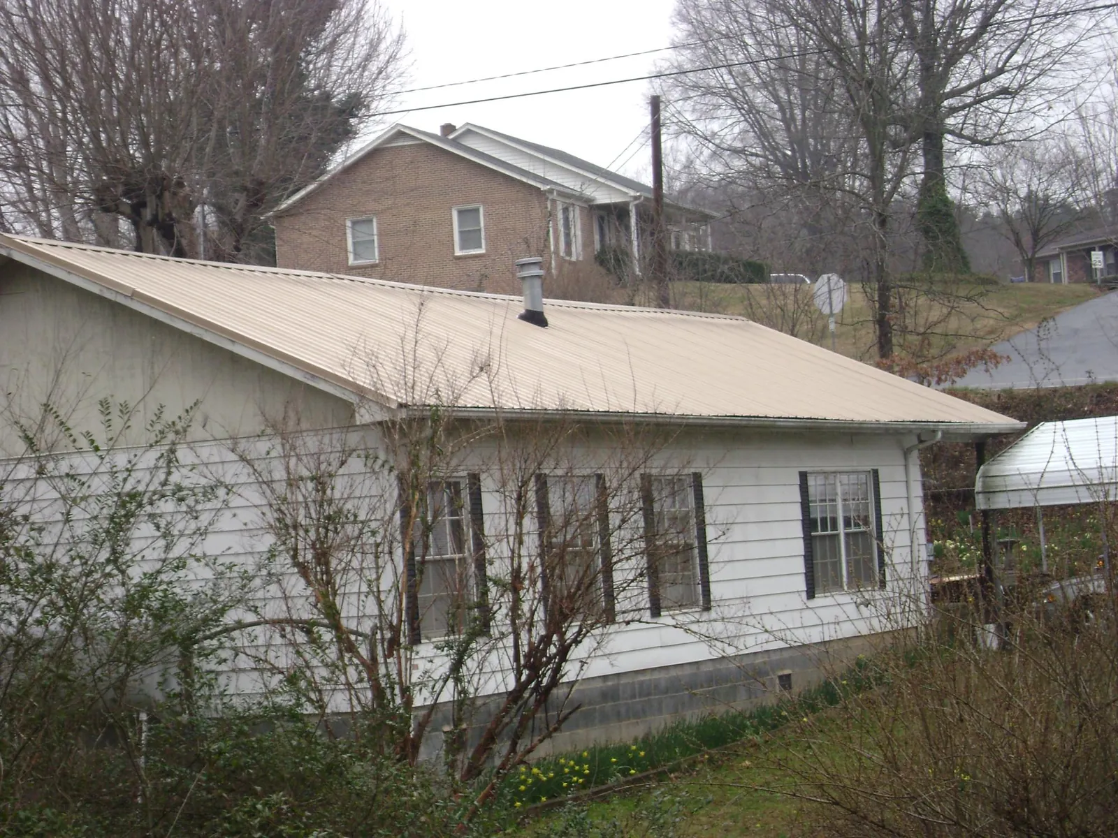 Tan metal roof on a white sided house set into a hillside — Commercial Roofing by Roofing Brothers in Gifford